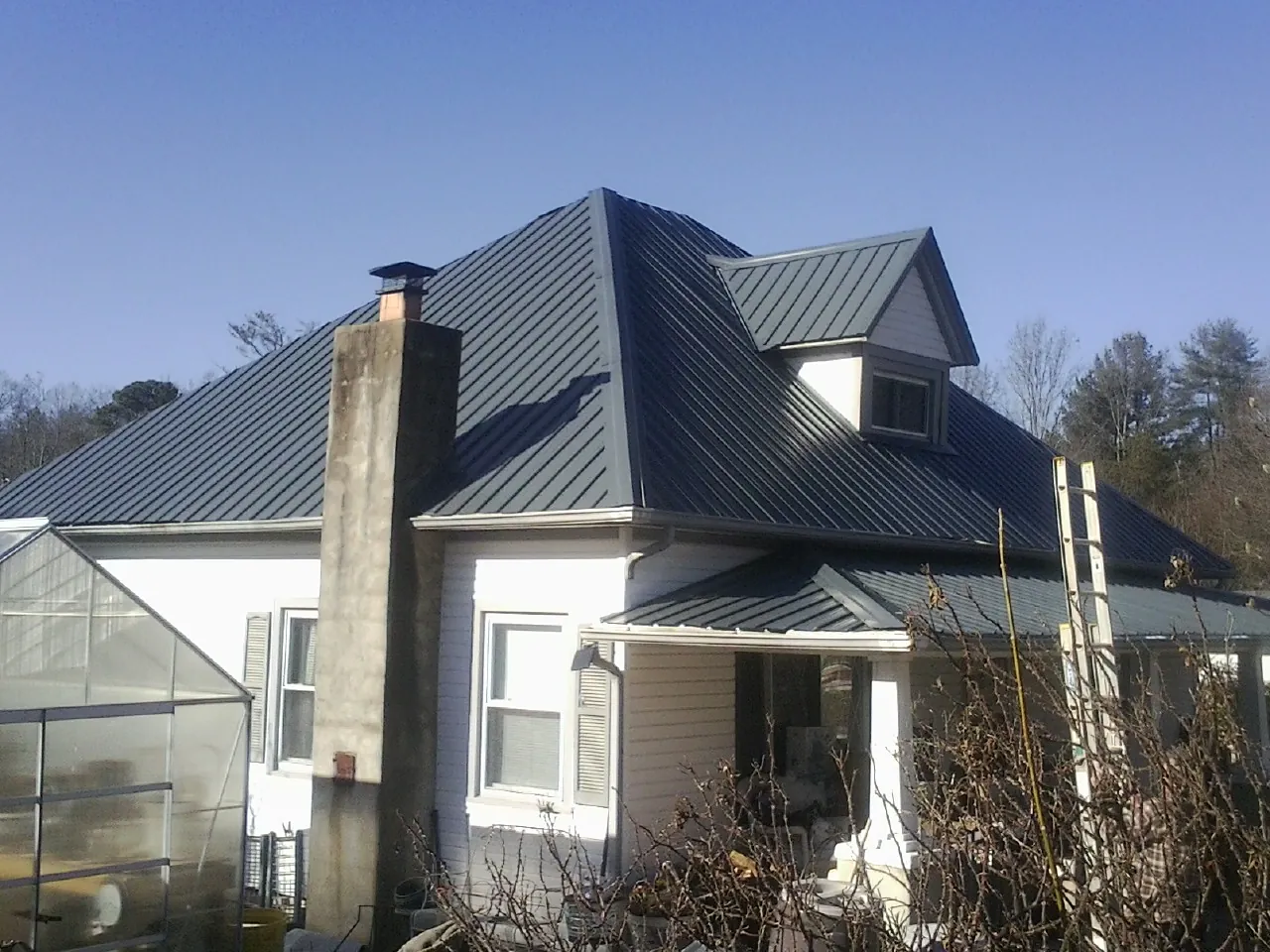 Dark blue standing seam metal roof on a white farmhouse with dormer — Slate & Tile Roof Repair by Roofing Brothers in Eagle Bend