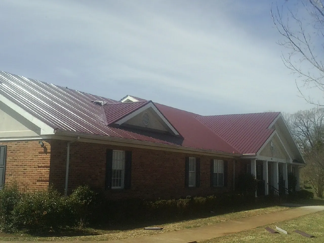 Red metal roof with gabled entries on a long brick building, from a Hail Damage Roof Repair job in Eagle Bend