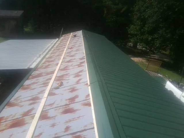 Old rusted panels beside newly installed green metal roofing — Wind Damage Roof Repair by Roofing Brothers in Eagle Bend