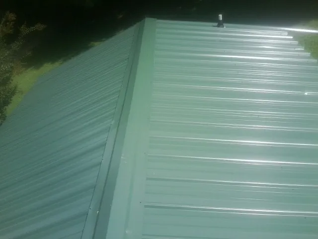 New green metal panels meeting at the ridge of a roof — Flat Roof Repair work by our crew in Eagle Bend