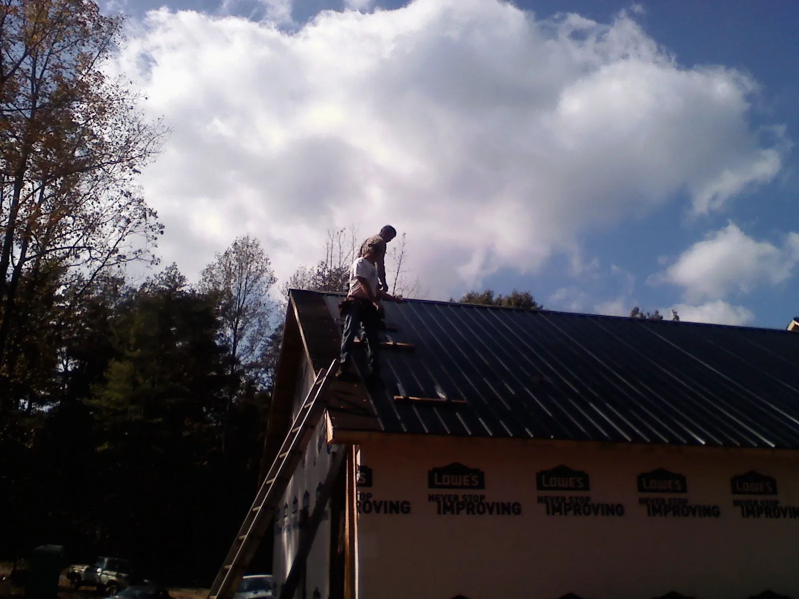 Roofer fastening dark metal panels high against a cloudy sky, from a Roof Inspection job in Eagle Bend