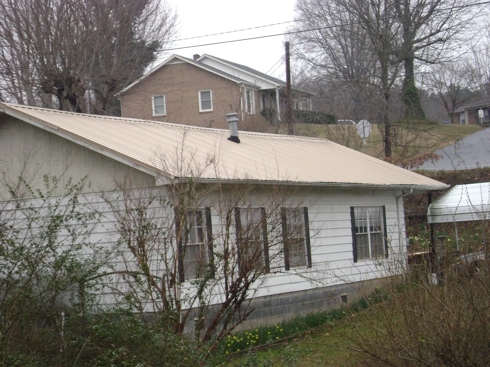 Tan metal roof on a white sided house set into a hillside — Commercial Roofing by Roofing Brothers in Eagle Bend