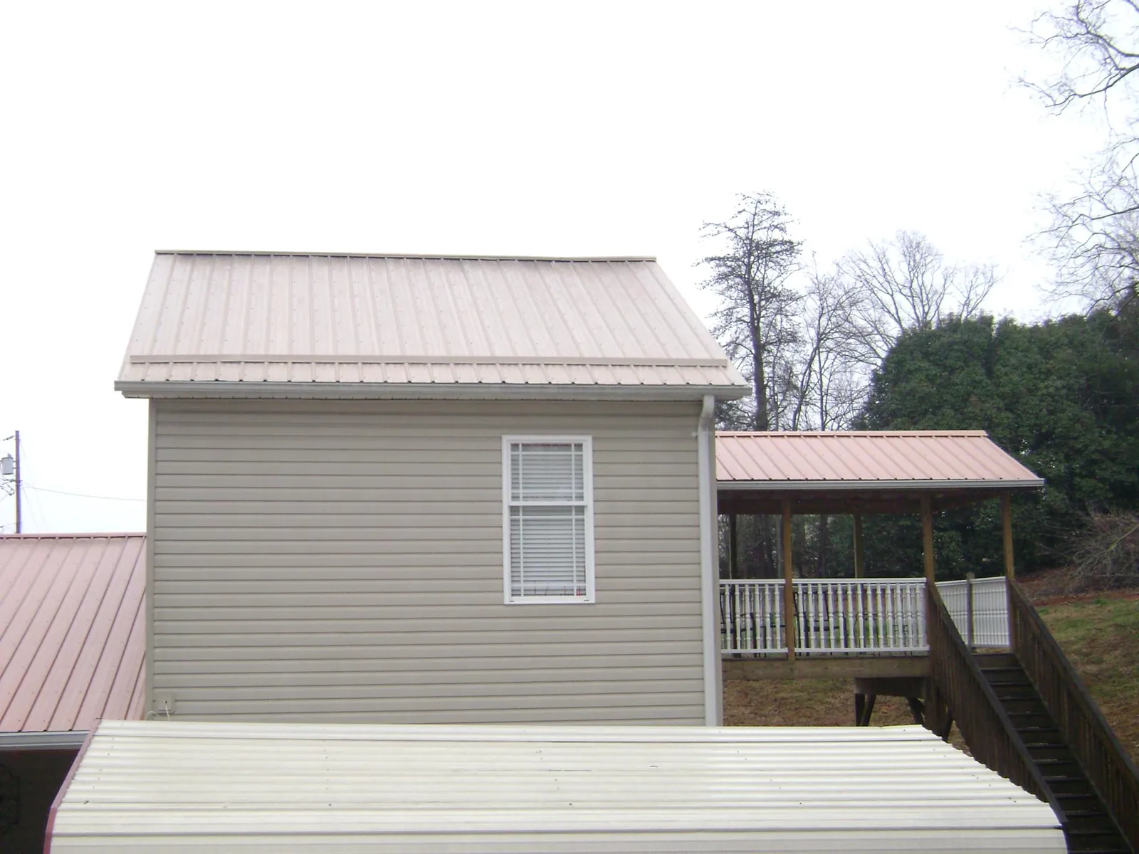 Tan metal roofs on a two story addition and attached porch, from a Roof Replacement job in Eagle Bend